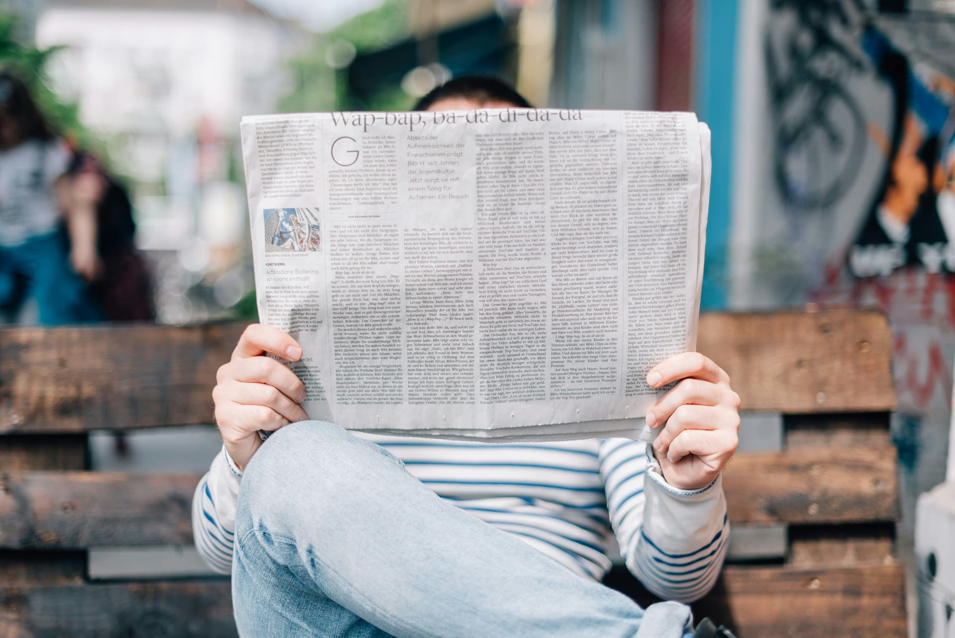 A person sits on a park bench holding a newspaper.